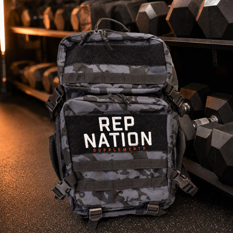 Rep Nation Tactical Bag 65L on the gym floor by the dumbbell rack